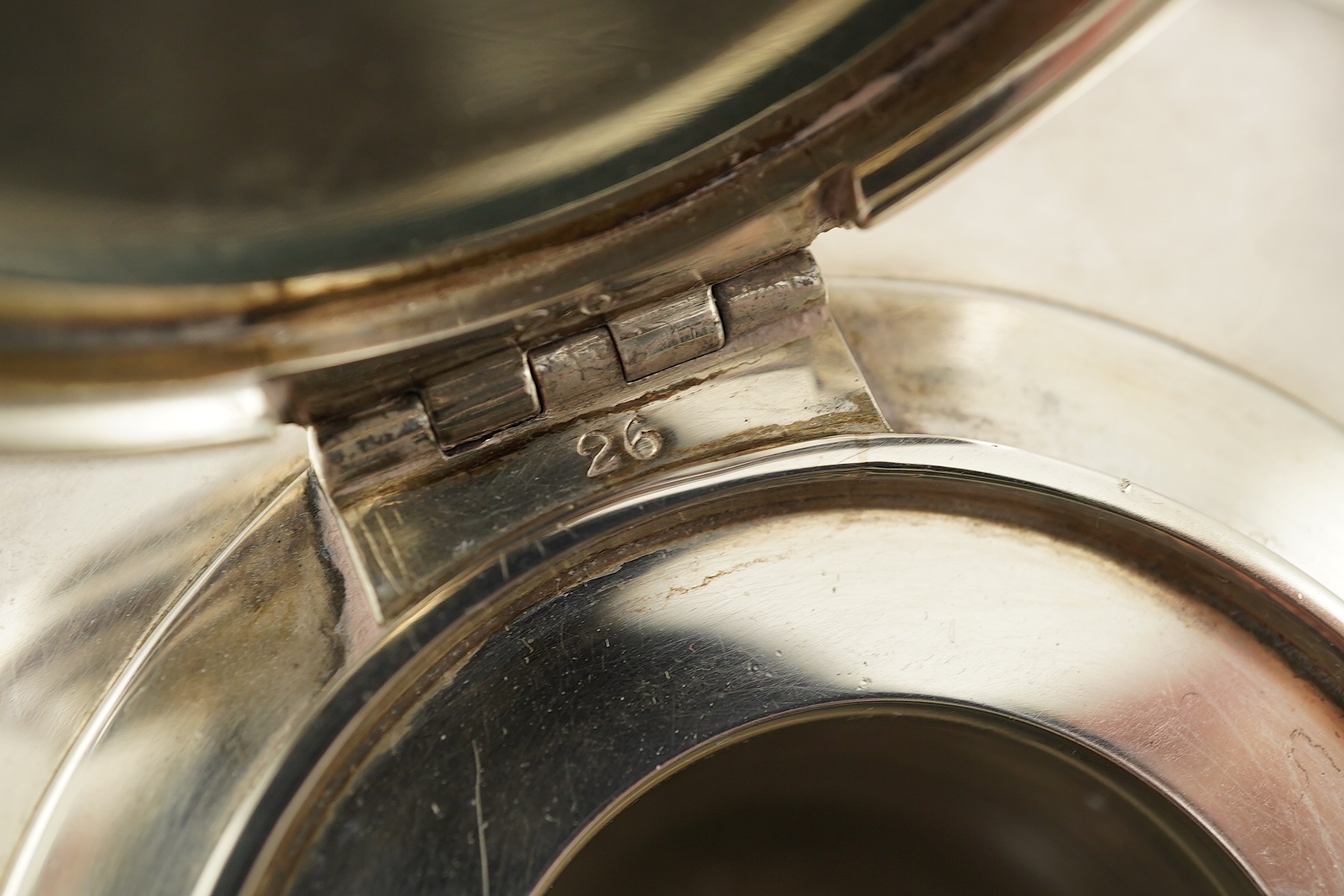 A George V silver circular inkwell, by Sebastian Garrard, commemorating the Silver Jubilee of King George V, the die stamped cover designed by George Kruger Gray featuring the Goldsmiths Company Coat of Arms